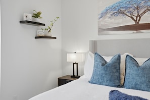 A bedroom with a bed, pillows, a nightstand, a lamp, a wall-mounted shelf with plants, and a painting. - 2 BR  2.5 Bathrooms Luxury Townhome <br>Prime Salt Lake City Location<br>Enjoy the perfect blend of convenience and comfort ~ Just 10 minutes from <br>Salt Lake Airport and 10 mins from Downtown SLC (North Salt Lake)