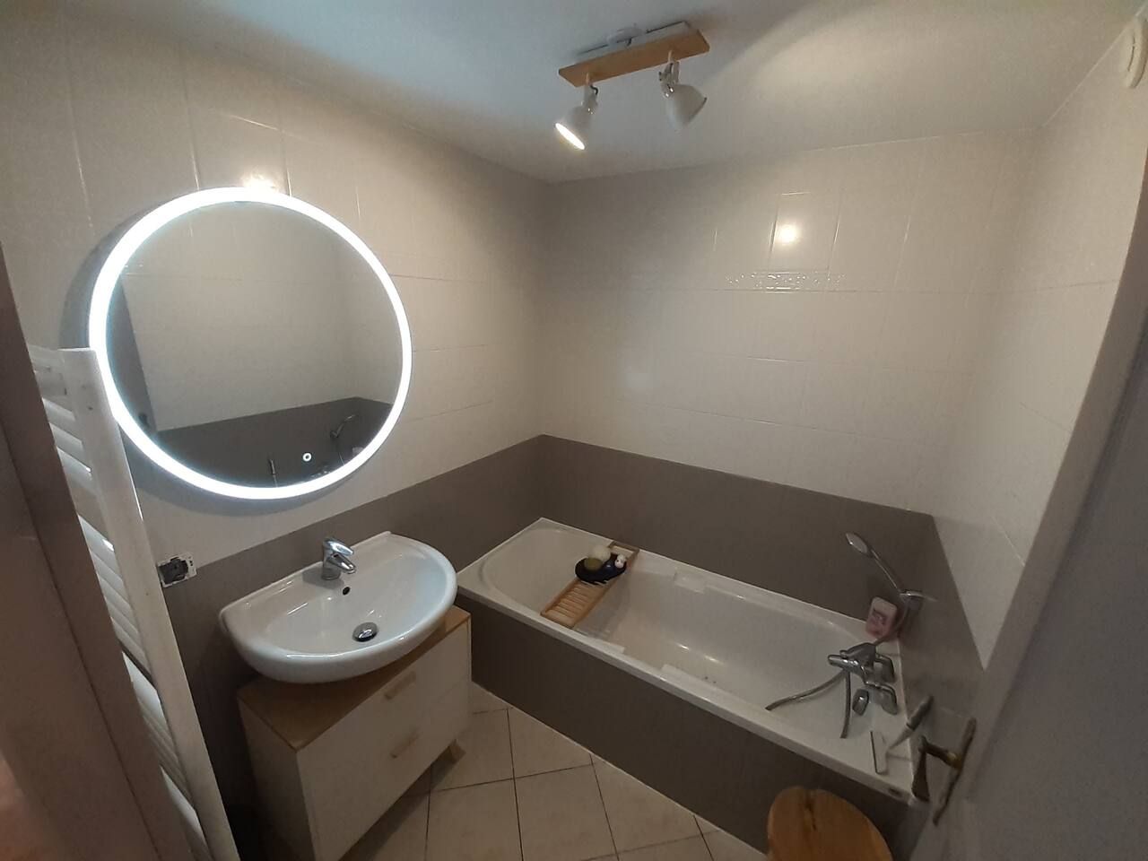 Une salle de bain avec un miroir rond, un lavabo et une baignoire.