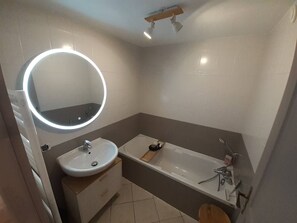 Une salle de bain avec un miroir rond, un lavabo et une baignoire.