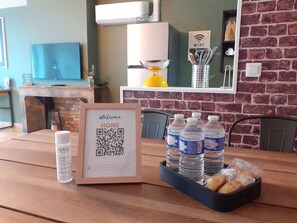 Une table à manger agrémentée d’un panneau d’accueil encadré, d’un code QR, de bouteilles d’eau et d’un panier à pain.