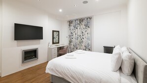 Un dormitorio moderno con cama, escritorio, chimenea y televisión.