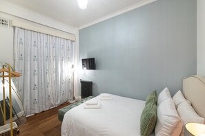 Ein Schlafzimmer mit einem Bett, Kissen, einem Heizkörper, einem Spiegel und einem Fenster mit Vorhängen.