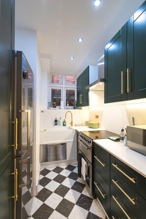 A kitchen with a black and white checkered floor, stainless steel appliances, and dark green cabinets with gold handles. - Luxurious & Spacious 2 Bed Basement Flat in South Kensington - Pass the Keys (London)