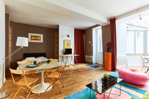 Une chambre moderne avec un lit, une table à manger et des chaises, un téléviseur et un fauteuil poire rose.