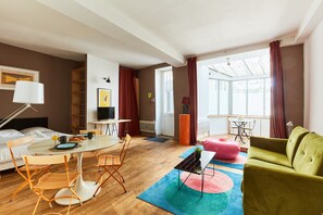 Une chambre d’hôtel moderne dotée d’un coin repas, d’un canapé, d’une télévision et d’une grande fenêtre avec des rideaux.
