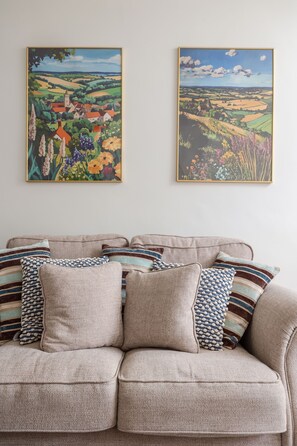 A beige sofa with striped pillows against a white wall, flanked by two landscape paintings.