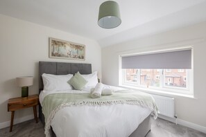 A bedroom with a bed, a nightstand, a lamp, a window with a view, and a painting on the wall.