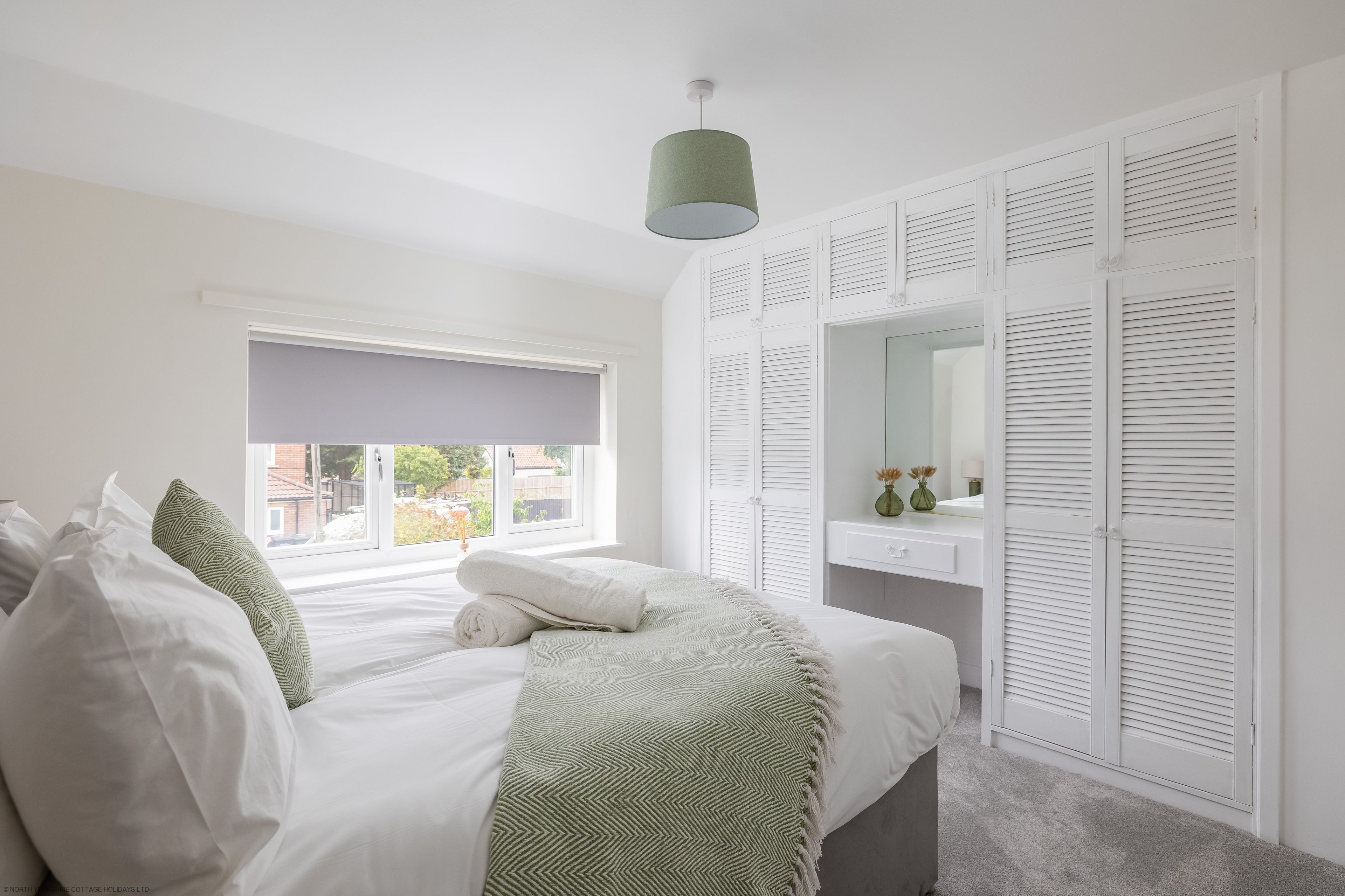 A bedroom with a bed, a window with a view, a wardrobe with louvered doors, and a hanging light fixture.