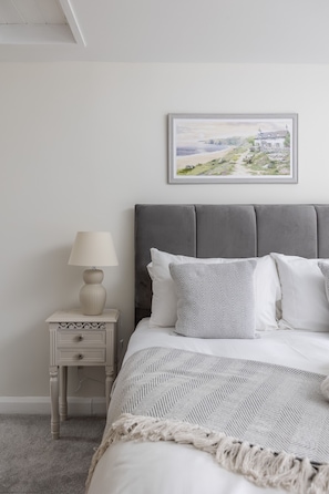 Un dormitorio con cama, mesita de noche, lámpara y un cuadro en la pared.