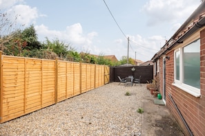 A backyard with a wooden fence, gravel ground, a brick house, and a table with chairs.