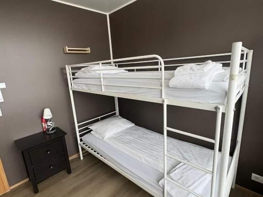 Uma cama beliche em quarto com parede escura e chão de madeira.