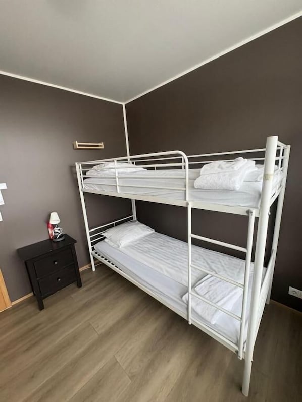 Una cama individual en literas en una habitación con pared oscura y suelo de madera.