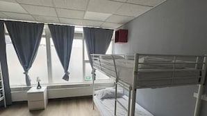 Ein Einzelzimmer mit Etagenbett, Nachttisch, Lampe und einem Fenster mit Vorhängen.