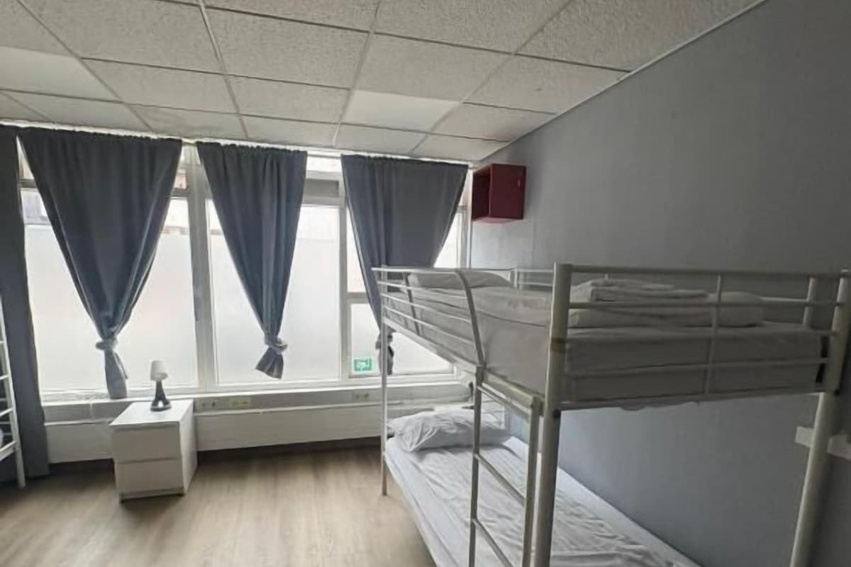 Ein Einzelzimmer mit Etagenbett, Nachttisch, Lampe und einem Fenster mit Vorhängen.