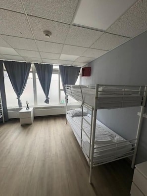 Une chambre individuelle avec un lit superposé, une table de chevet, une lampe et une fenêtre avec des rideaux.