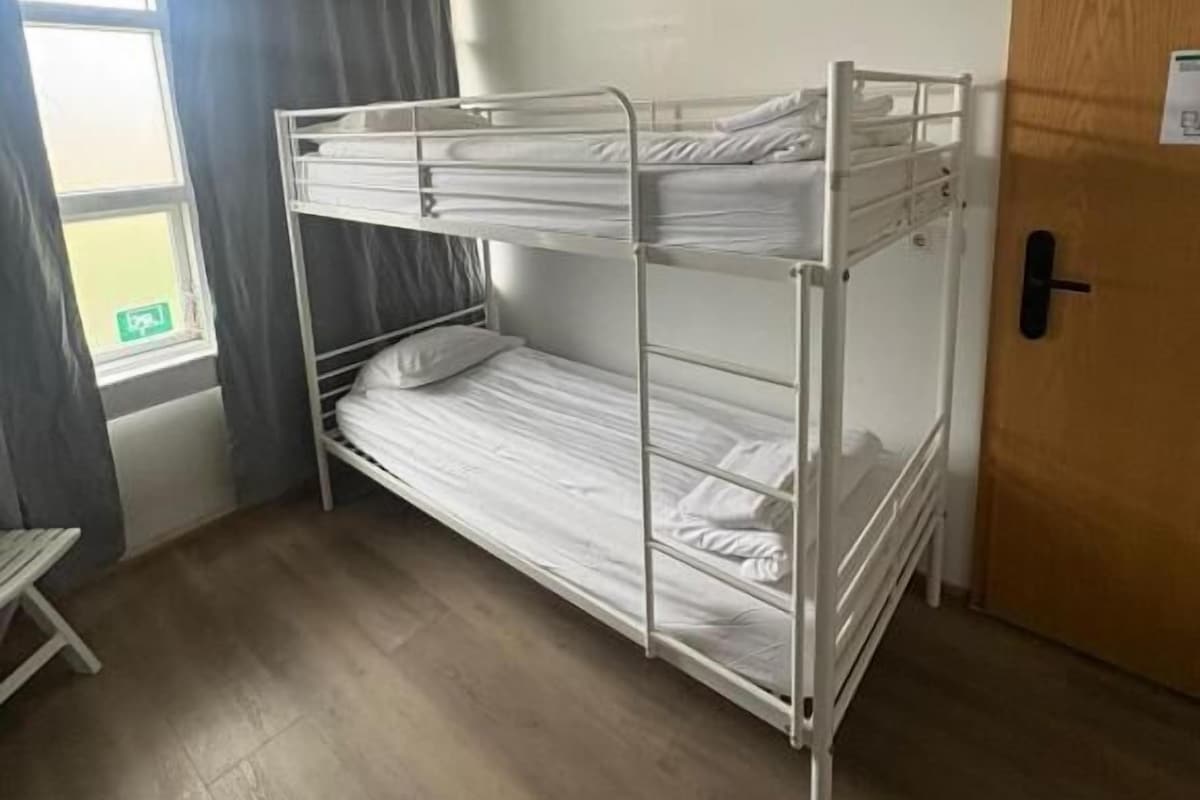 Ein Schlafraum mit Etagenbetten, einem Fenster, einer Tür und einem kleinen Tisch.