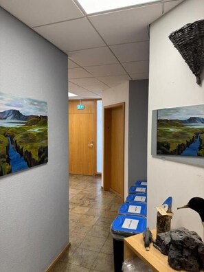 A hallway with paintings on the walls, a wooden door, and a desk with a bird sculpture.