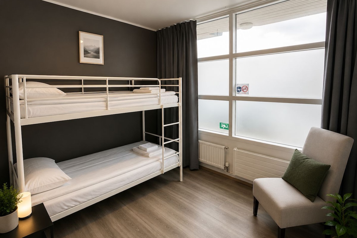 A bunk bed room with a window, a radiator, a chair, and a plant.