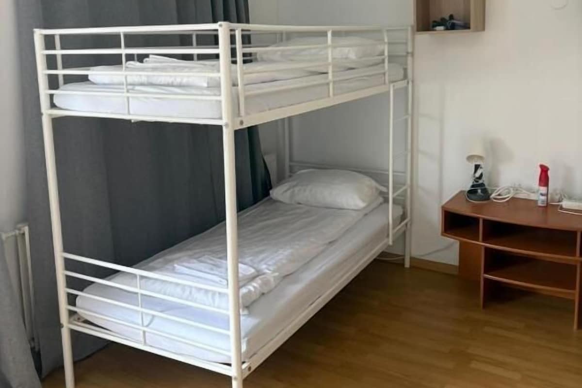 Ein Stockbett in einem Zimmer mit Holzboden, Schreibtisch und kleinen Regal.