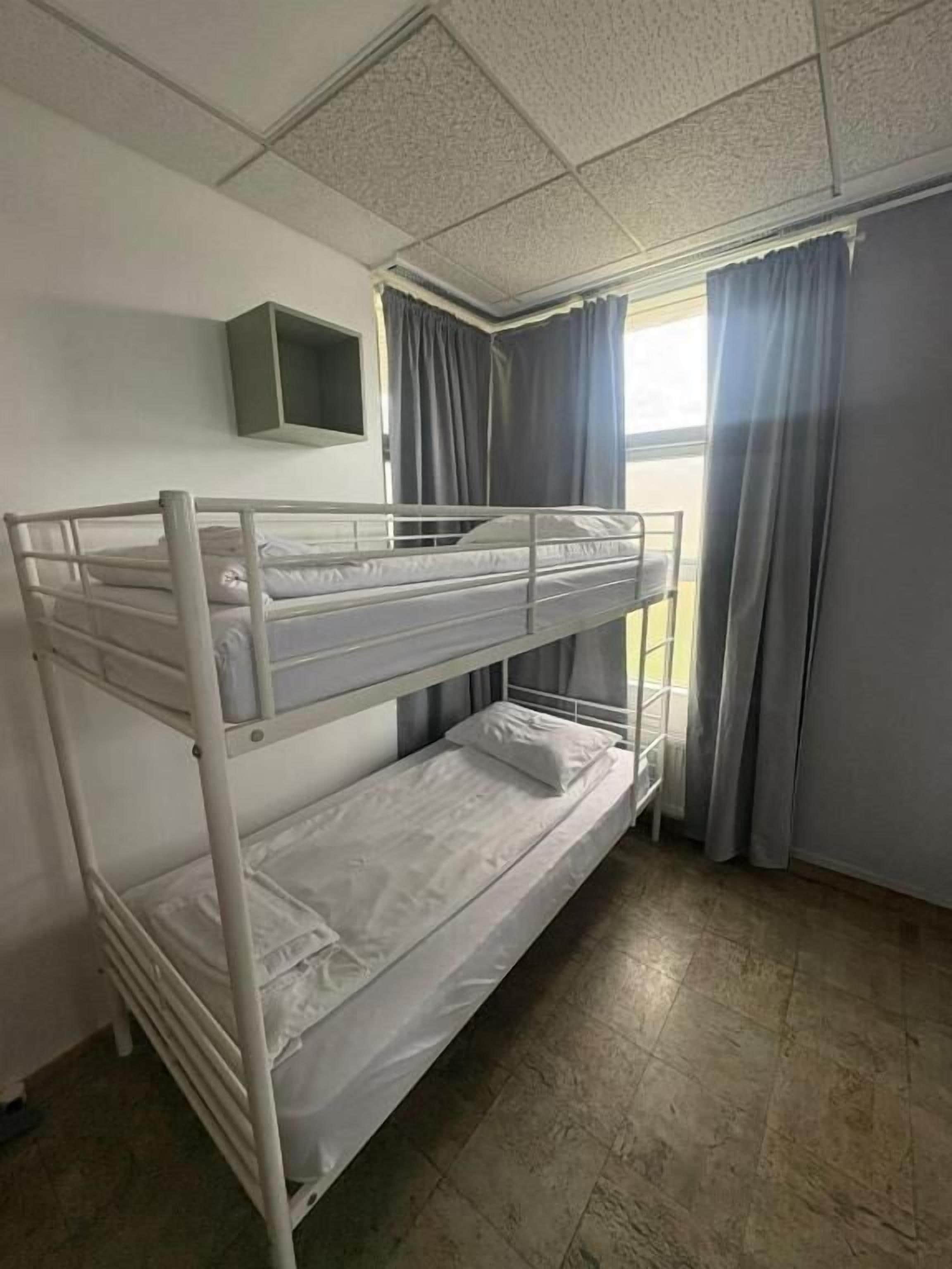 Ein Schlafraum mit Etagenbetten, einem Fernseher an der Wand, Vorhängen am Fenster und einem Fliesenboden.