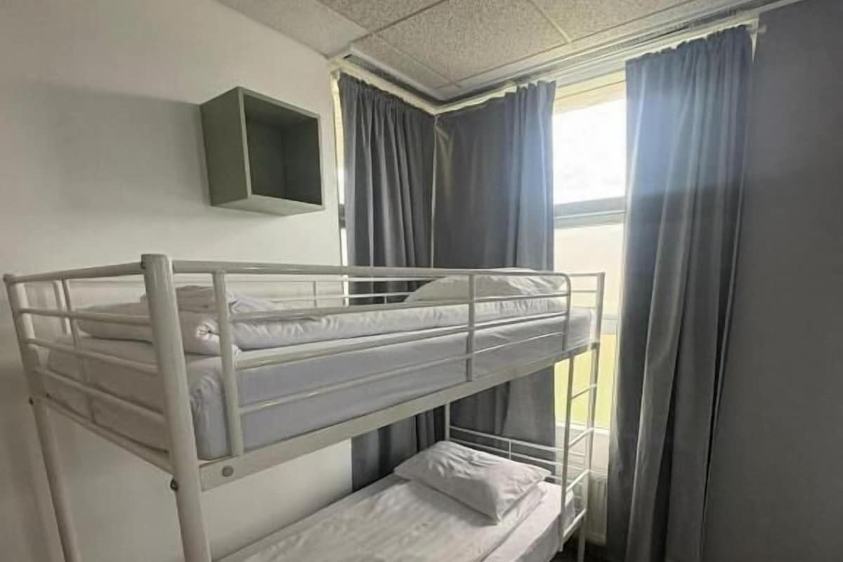 Ein Schlafraum mit Etagenbetten, einem Fernseher an der Wand, Vorhängen am Fenster und einem Fliesenboden.