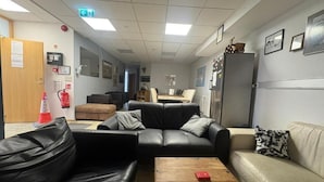 Ein Zimmer mit einer schwarzen Ledersofa, einem beigen Sofa, einem Holztisch und einem Kühlschrank.