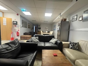 Une pièce comprenant un canapé en cuir noir, un canapé beige, une table basse en bois et un réfrigérateur.