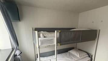 A bunk bed in a room with a window, a ceiling light, and wooden flooring.
