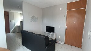 Ein Wohnzimmer mit einer schwarzen Couch, einem Fernseher auf einem Schrank, einer Holztür und einem Fliesenboden.