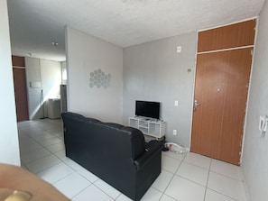 A living room with a black sofa, a television on a stand, a wooden door, and a tiled floor. - Apartment with two bedrooms in the bedroom (Macapá)