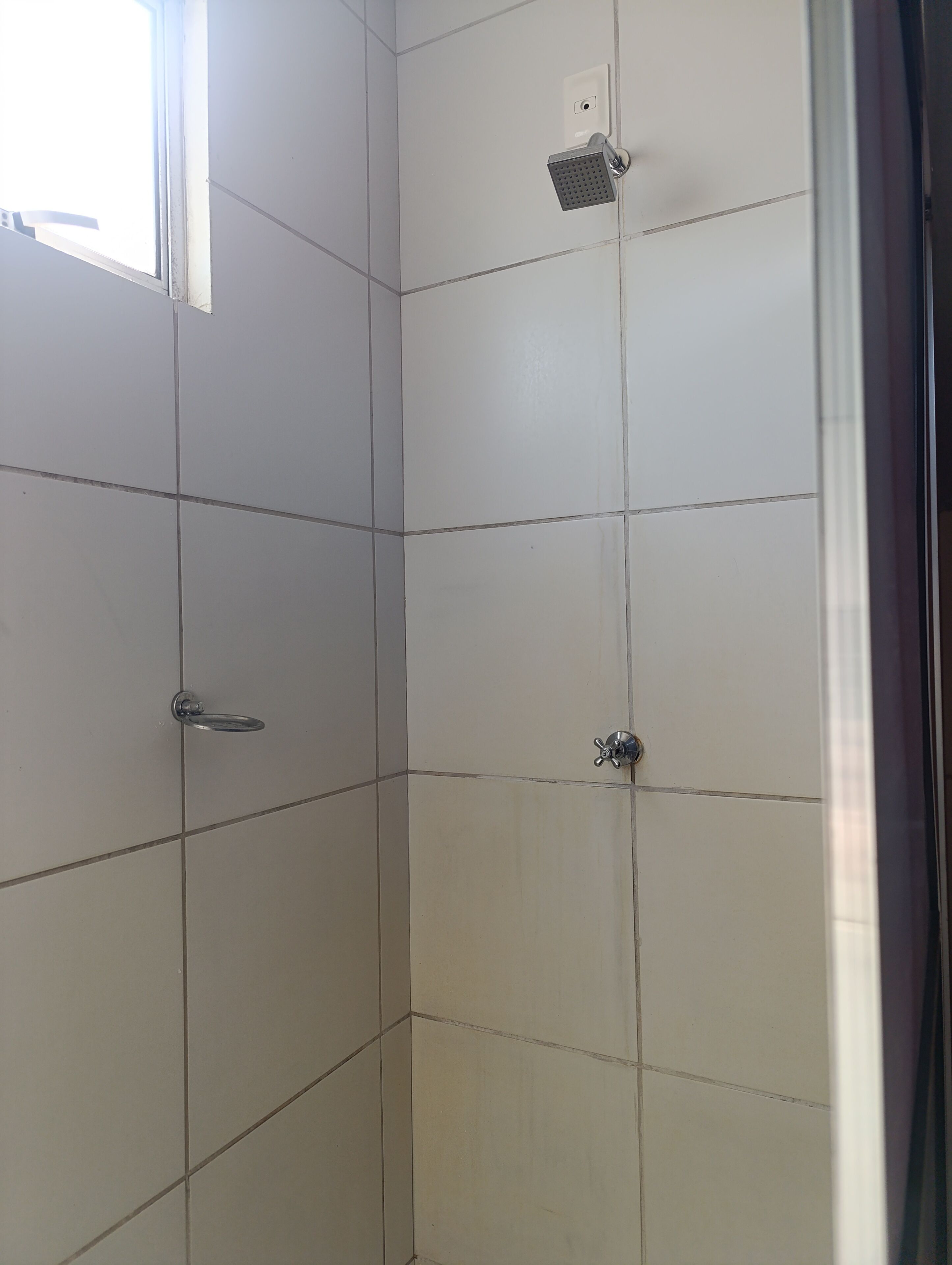 Box de chuveiro revestido com azulejos, com chuveiro manual e painel de controle.