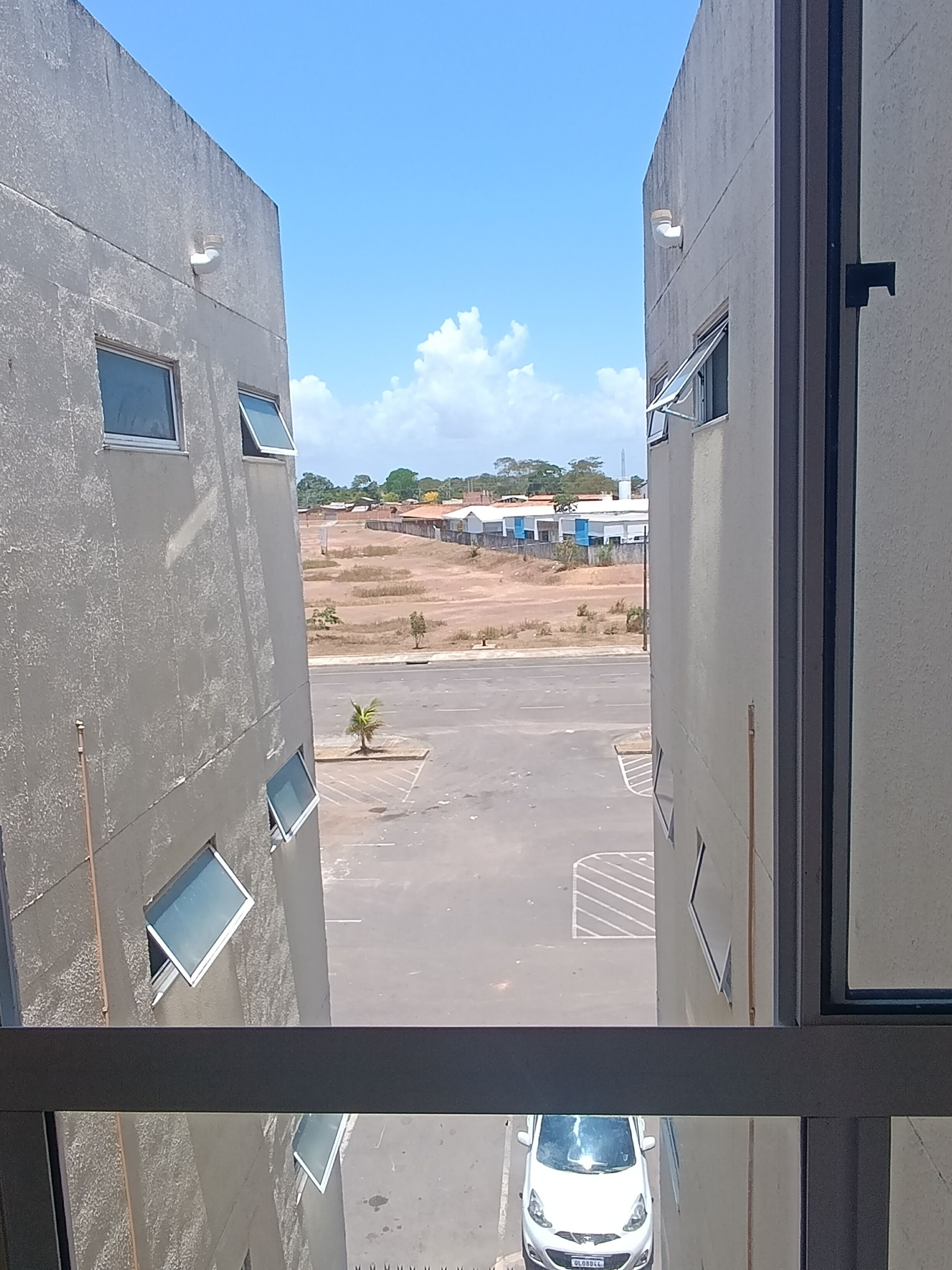 A view from inside a building looking out to a parking lot with a car, a small palm tree, and distant buildings.