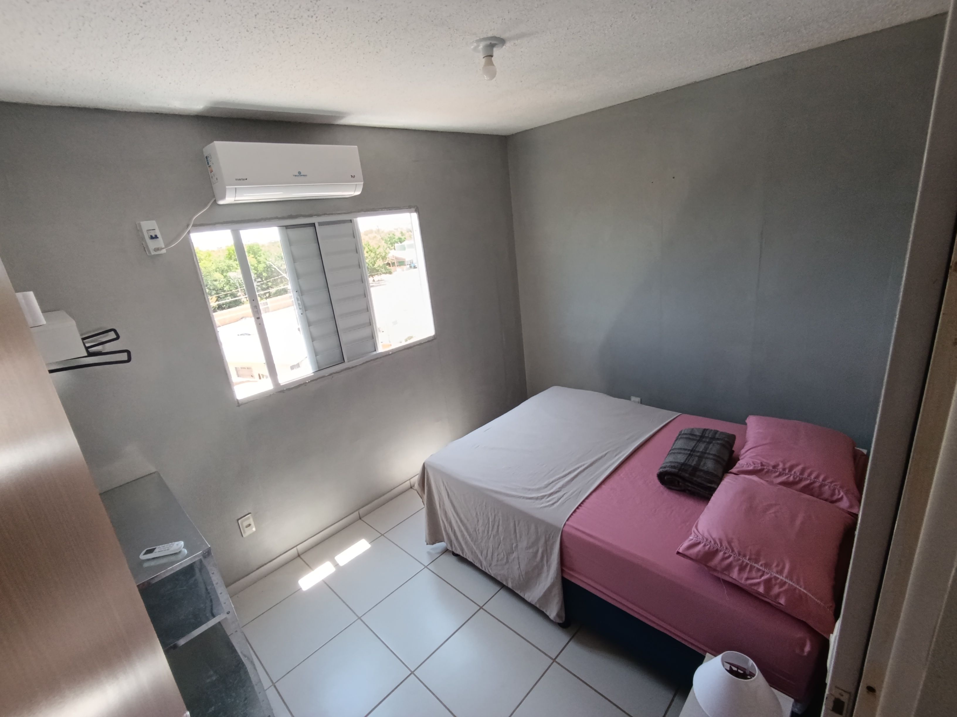 A bedroom with a bed, a window, and an air conditioning unit.