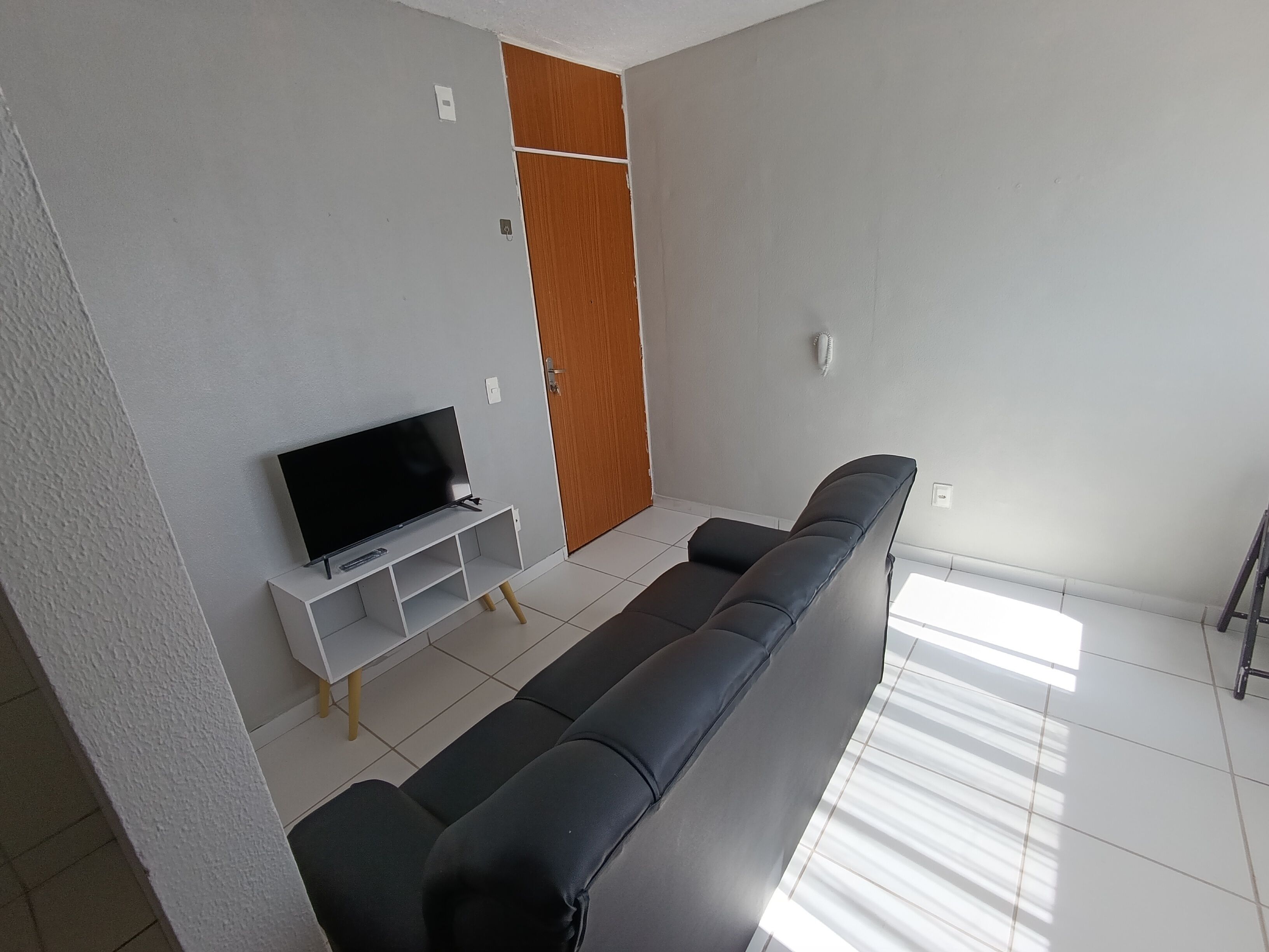 Uma sala de estar moderna com um sofá preto, uma televisão sobre um suporte branco e uma porta de madeira.