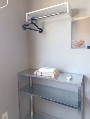 A bathroom with a metal shelf holding towels and a remote control, a towel rack, and a decorative item on the wall. - Apartment with two bedrooms in the bedroom (Macapá)