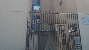 Ein Gebäude mit einem verschlossenen Eingangsbereich, einem Schild mit der Aufschrift 'Bloco 60' und einem kleinen Garten mit Blumen.