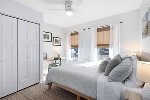 Ein Schlafzimmer mit Bett, Schreibtisch und Stuhl. Zwei Fenster mit Vorhängen bieten einen Ausblick nach draußen.