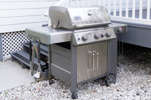 Un barbecue portable en acier inoxydable, doté de quatre boutons de contrôle et d’un thermomètre intégré, placé sur une surface recouverte de gravier.
