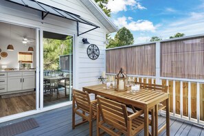 Eine Holzterrasse mit Tisch und Stühlen, eine weiße Außenwand und ein Fenster mit Blick auf einen Garten.