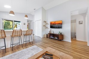 Ein modernes Wohnzimmer mit Holzboden, einer Bar mit Korbstühlen, einem an der Wand befestigten Flachbildfernseher und einem Bücherregal.