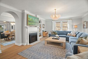Una sala de estar con chimenea, un candelabro, un sofá azul y un comedor con mesa y sillas.