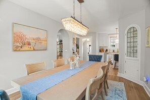 A dining area with a long table, chairs, a chandelier, and a painting on the wall. - MINNeSTAY * Rose Garden Retreat (Minneapolis)