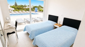 A hotel room with two beds, a desk, a chair, a small table, and a view of a swimming pool. - Villa Carvoeiro, luxury 10 Bedroom, heated pool, games, BBQ (Carvoeiro)