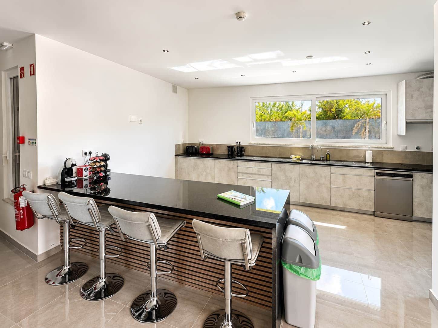 Una cocina moderna con una isla central, taburetes de bar y vistas al exterior.