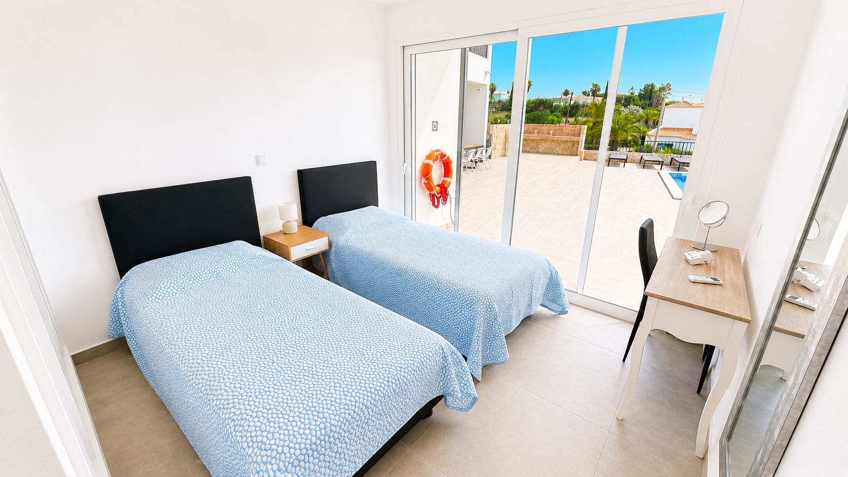 A hotel room with two beds, a desk, and a view of a swimming pool.