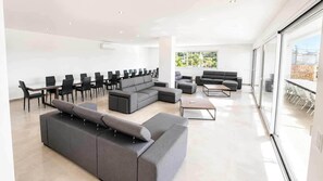 A spacious, modern lounge area with a long dining table, multiple sofas, and chairs arranged for socializing. - Villa Carvoeiro, luxury 10 Bedroom, heated pool, games, BBQ (Carvoeiro)