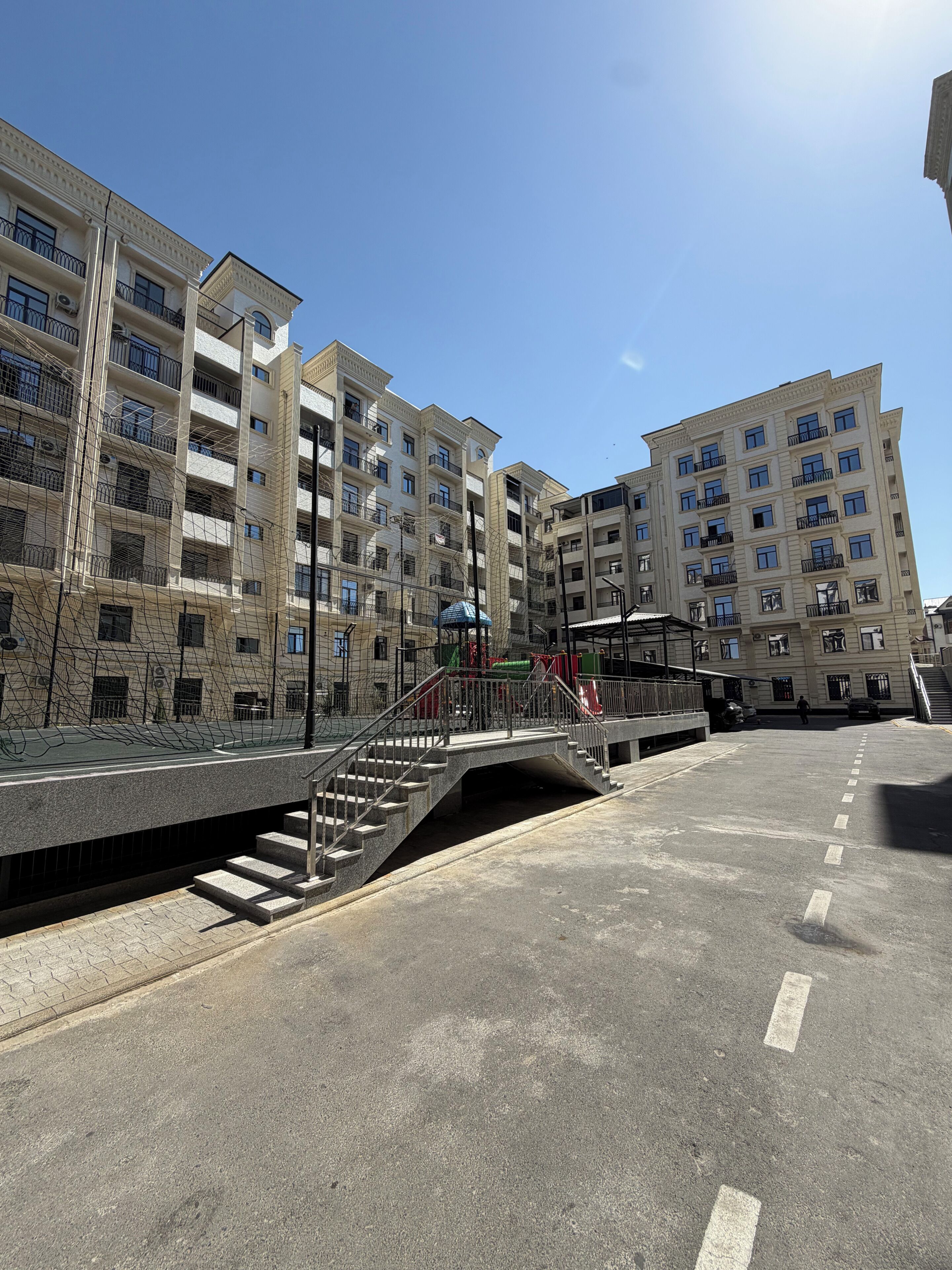 A multi-story residential building with balconies, a pedestrian bridge, and a playground.