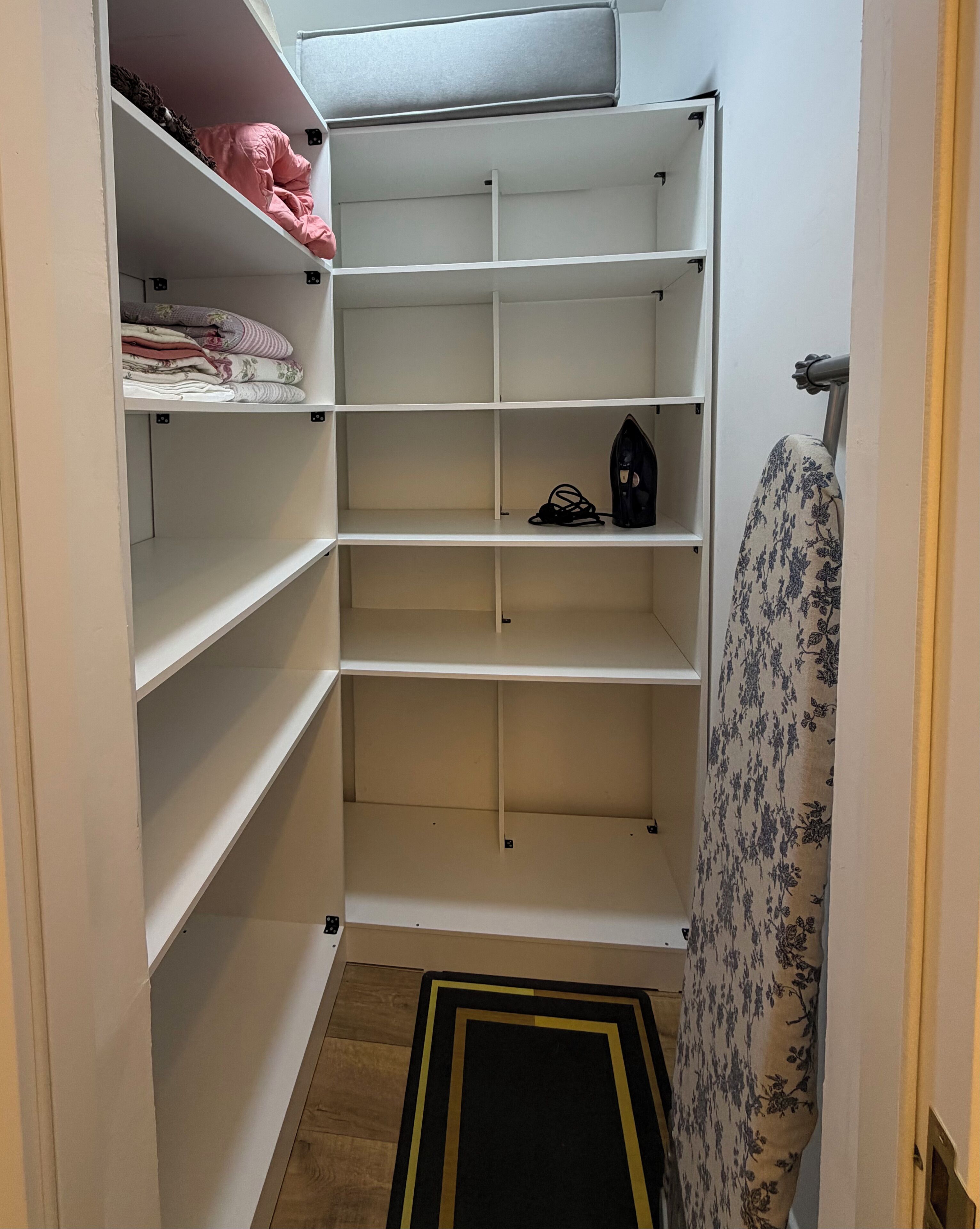 A closet with multiple shelves, some with folded clothes, and a black bag on one shelf.