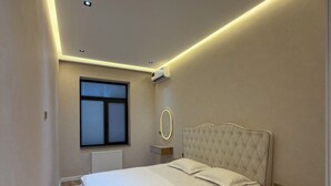 Ein Schlafzimmer mit einem Bett, Nachttischen, einem Fenster und einer Deckenleuchte.