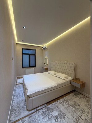 Ein Schlafzimmer mit einem Bett, Nachttischen, einem Fenster und einer Deckenleuchte.